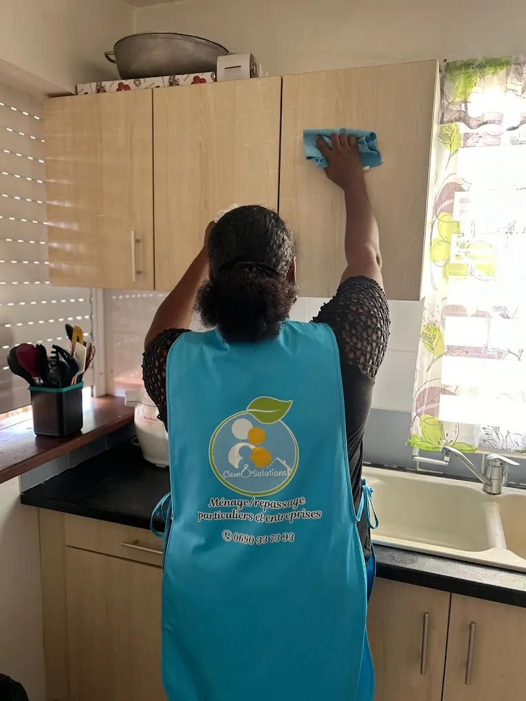 Intervenante Clean & Solutions en tablier floqué au logo, nettoyant les placards d'une cuisine chez un particulier en Guadeloupe